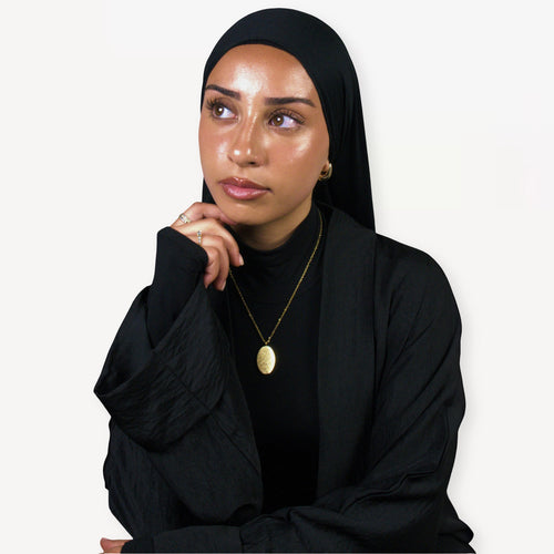 Woman wearing a black hijab and black outfit with a gold ayatul kursi necklace on a white background