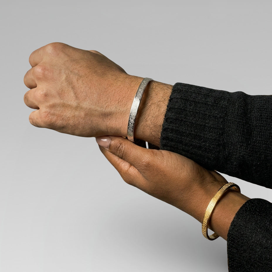 Two hands wearing Cairo's silver and gold Ayatul kursi bracelets on a gray background